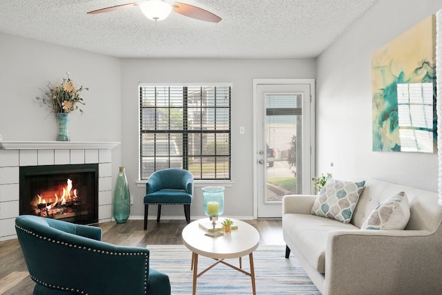 living room with a tile fireplace, wood-type flooring, a textured ceiling, and ceiling fan