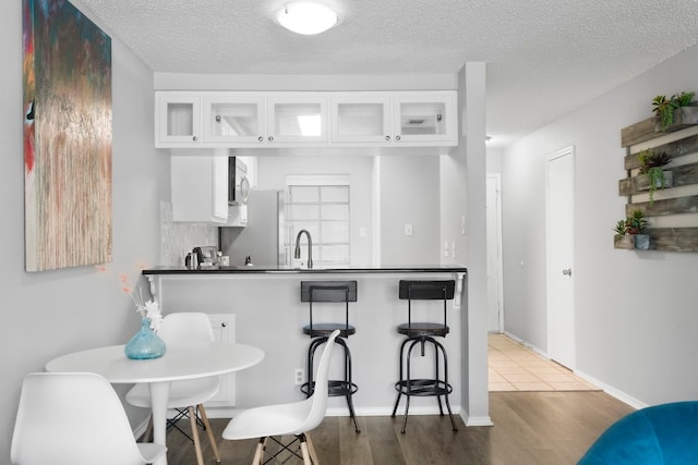 kitchen featuring wood-type flooring, a textured ceiling, sink, white cabinets, and a kitchen breakfast bar