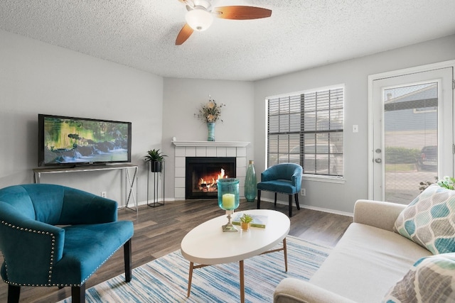 living room featuring a tiled fireplace, ceiling fan, dark wood-type flooring, and a textured ceiling