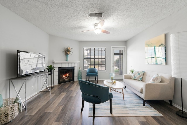 living room with a textured ceiling, a fireplace, ceiling fan, and dark wood-type flooring