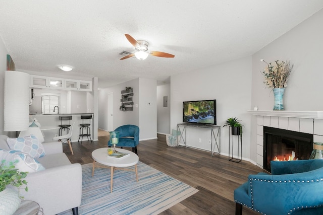 living room with a textured ceiling, sink, a fireplace, dark hardwood / wood-style flooring, and ceiling fan