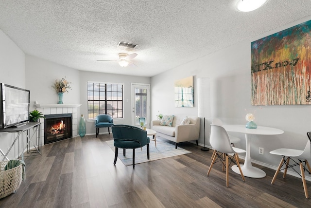 living room featuring a textured ceiling, a tile fireplace, ceiling fan, and dark wood-type flooring