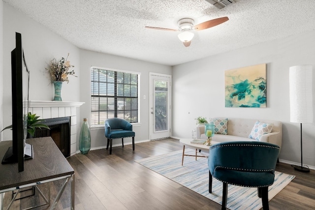 interior space with a textured ceiling, a tiled fireplace, ceiling fan, and dark hardwood / wood-style flooring