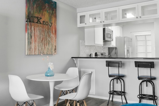 kitchen with tasteful backsplash, a textured ceiling, white cabinetry, stainless steel appliances, and dark hardwood / wood-style floors