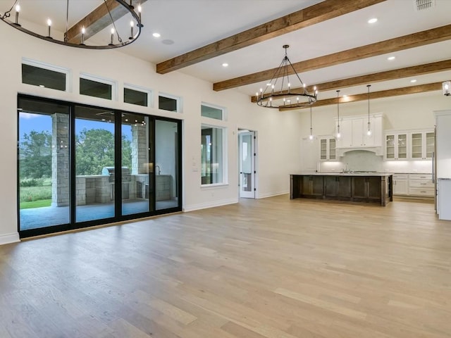 unfurnished living room with beamed ceiling, a notable chandelier, and light hardwood / wood-style flooring