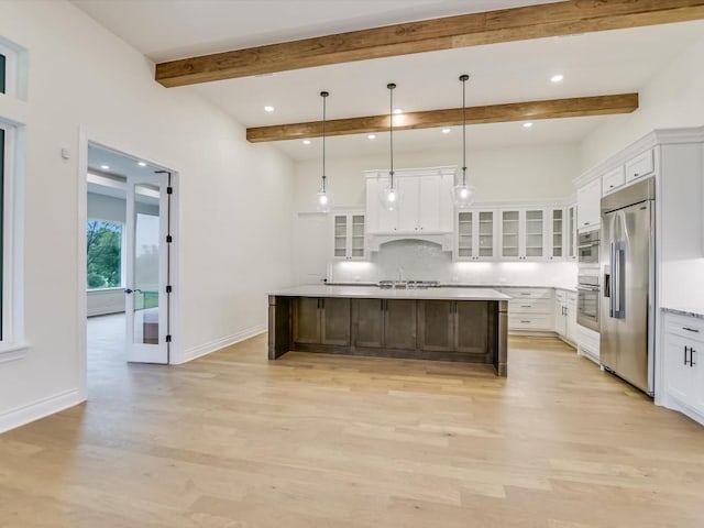 kitchen with light hardwood / wood-style flooring, appliances with stainless steel finishes, hanging light fixtures, white cabinets, and a large island with sink