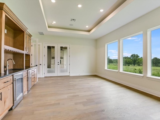 interior space featuring sink, french doors, wine cooler, a tray ceiling, and light brown cabinetry