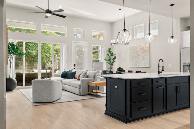 kitchen with a center island with sink, sink, light hardwood / wood-style floors, ceiling fan with notable chandelier, and a towering ceiling