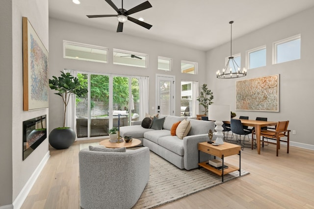 living room featuring ceiling fan with notable chandelier, light hardwood / wood-style floors, and a towering ceiling