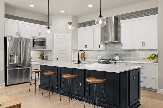 kitchen featuring wall chimney range hood, light hardwood / wood-style floors, appliances with stainless steel finishes, and backsplash