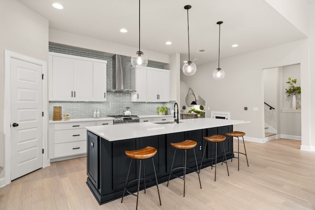 kitchen featuring wall chimney range hood, sink, a kitchen island with sink, and light wood-type flooring