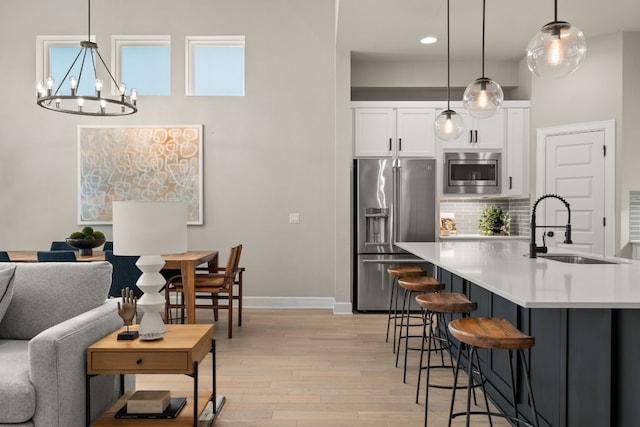 kitchen featuring hanging light fixtures, sink, light hardwood / wood-style floors, appliances with stainless steel finishes, and backsplash