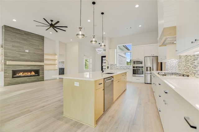 kitchen with light hardwood / wood-style flooring, stainless steel appliances, a kitchen island with sink, a tile fireplace, and backsplash