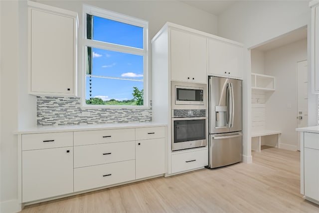 kitchen featuring white cabinets, light wood-type flooring, backsplash, and appliances with stainless steel finishes