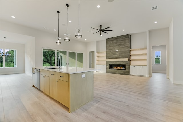 kitchen with a center island with sink, sink, a tiled fireplace, and light wood-type flooring