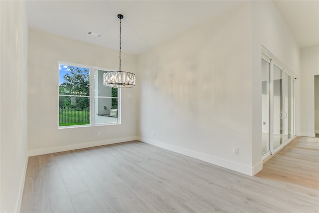 spare room with a notable chandelier and light hardwood / wood-style floors