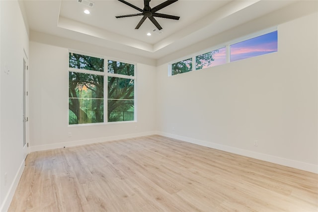 spare room featuring ceiling fan, light hardwood / wood-style flooring, and a raised ceiling