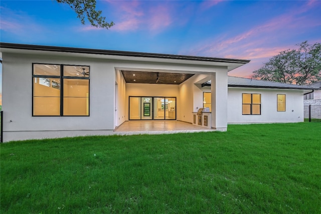 back house at dusk featuring a patio area and a lawn