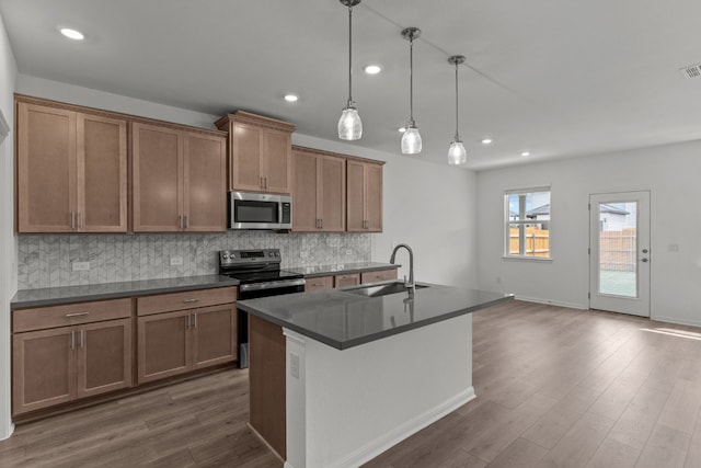 kitchen with dark wood-type flooring, hanging light fixtures, a center island with sink, sink, and appliances with stainless steel finishes