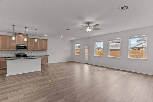 kitchen with ceiling fan, appliances with stainless steel finishes, an island with sink, light hardwood / wood-style flooring, and decorative light fixtures