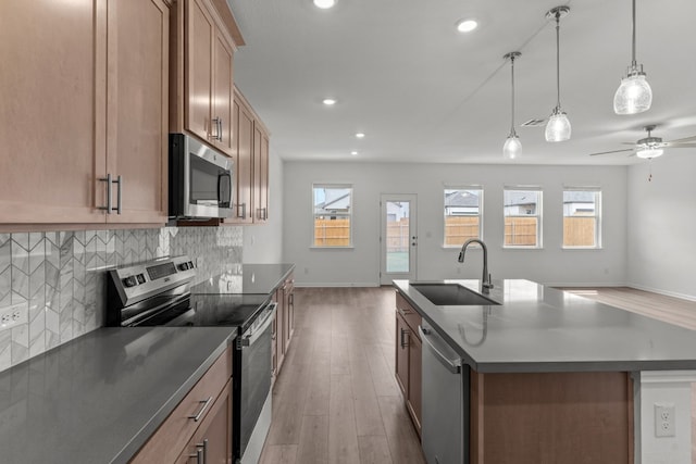 kitchen featuring hardwood / wood-style floors, appliances with stainless steel finishes, a kitchen island with sink, pendant lighting, and sink