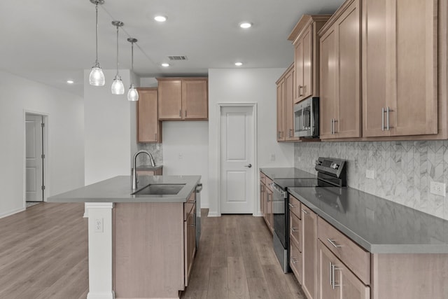 kitchen with sink, stainless steel appliances, pendant lighting, light hardwood / wood-style flooring, and a center island with sink