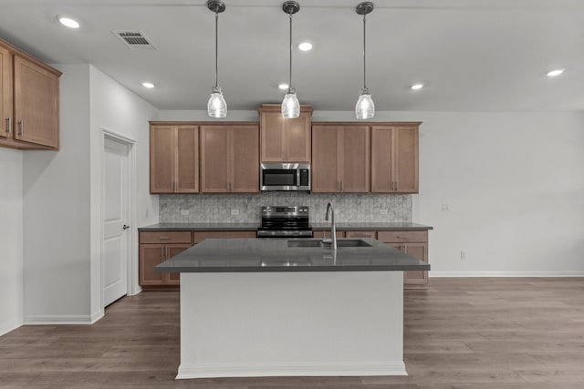 kitchen with a center island with sink, pendant lighting, stainless steel appliances, and wood-type flooring