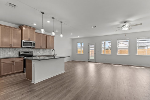 kitchen featuring backsplash, ceiling fan, an island with sink, hardwood / wood-style flooring, and pendant lighting