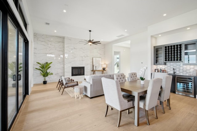 dining room with light hardwood / wood-style flooring, ceiling fan, a fireplace, wet bar, and beverage cooler