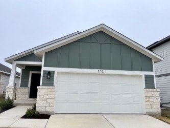 view of front of house with an attached garage, stone siding, driveway, and board and batten siding