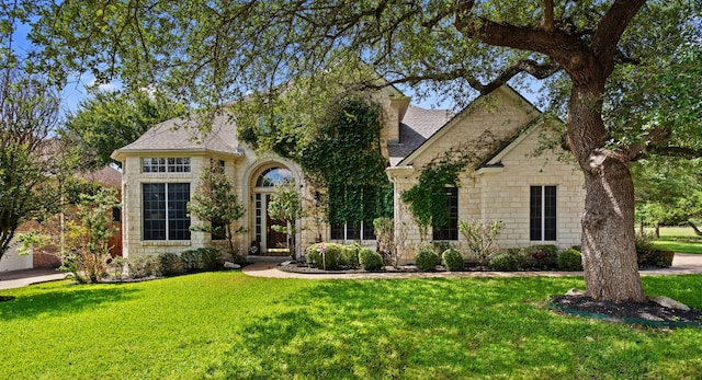 view of front facade featuring a shingled roof, stone siding, and a front lawn