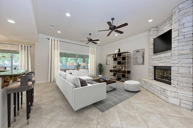 tiled living room with ceiling fan, ornamental molding, and a stone fireplace