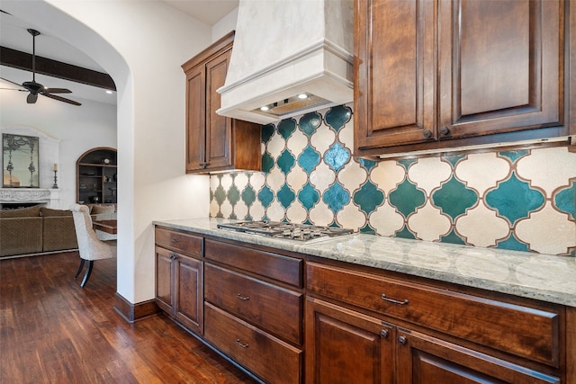 kitchen featuring stainless steel gas stovetop, ceiling fan, custom range hood, tasteful backsplash, and dark hardwood / wood-style flooring