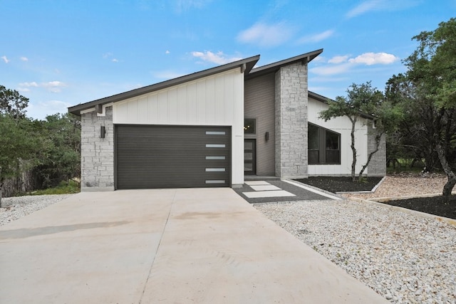 view of front of property featuring driveway, stone siding, board and batten siding, and an attached garage