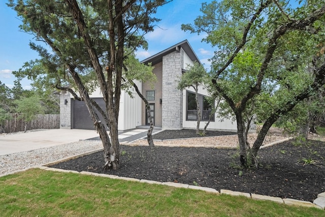 view of front of house with stone siding, concrete driveway, fence, and an attached garage