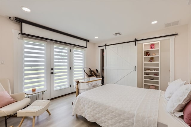 bedroom with a barn door, access to exterior, and light wood-type flooring