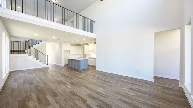 unfurnished living room with hardwood / wood-style flooring, a towering ceiling, and sink