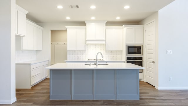 kitchen with stainless steel oven, white cabinets, a kitchen island with sink, and sink