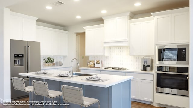 kitchen with appliances with stainless steel finishes, a breakfast bar area, white cabinetry, and an island with sink