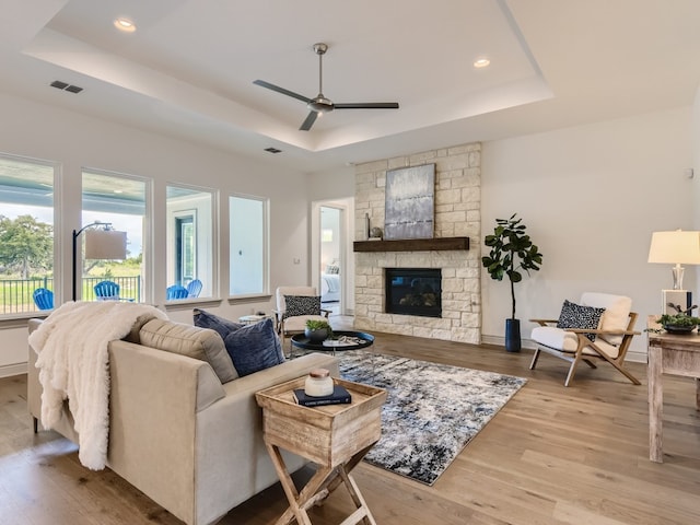 living room featuring ceiling fan, light hardwood / wood-style flooring, a fireplace, and a raised ceiling