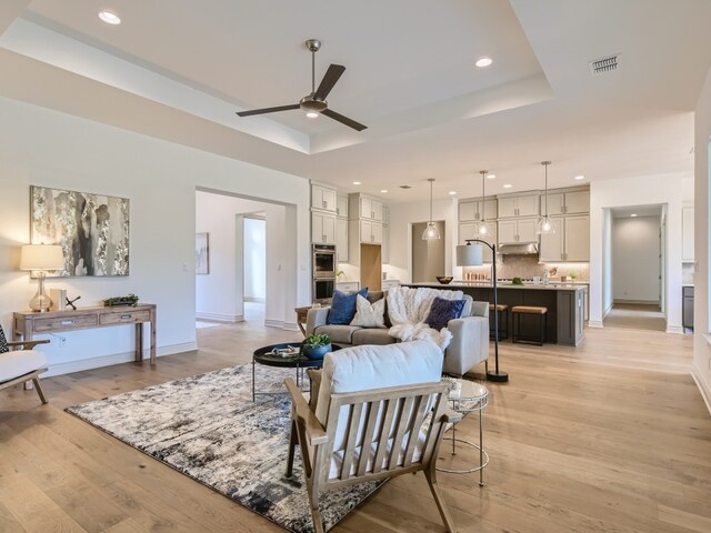 living room featuring ceiling fan, a raised ceiling, and light hardwood / wood-style floors