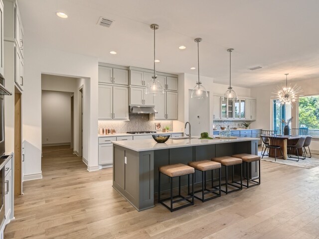 kitchen featuring decorative backsplash, a kitchen island with sink, pendant lighting, and light hardwood / wood-style floors