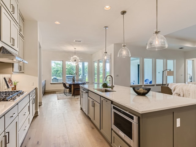 kitchen featuring a center island with sink, light hardwood / wood-style floors, sink, stainless steel gas cooktop, and decorative light fixtures