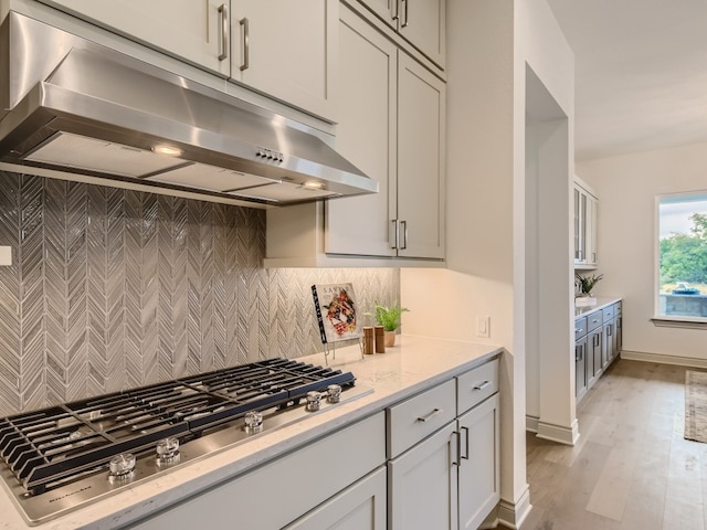 kitchen with gray cabinets, backsplash, light stone counters, light hardwood / wood-style flooring, and stainless steel gas cooktop