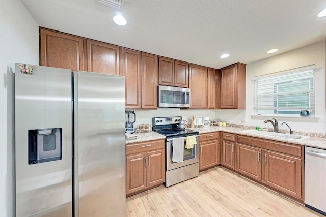 kitchen featuring light stone counters, appliances with stainless steel finishes, light hardwood / wood-style floors, and sink