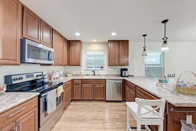 kitchen featuring decorative light fixtures, sink, light hardwood / wood-style floors, appliances with stainless steel finishes, and kitchen peninsula