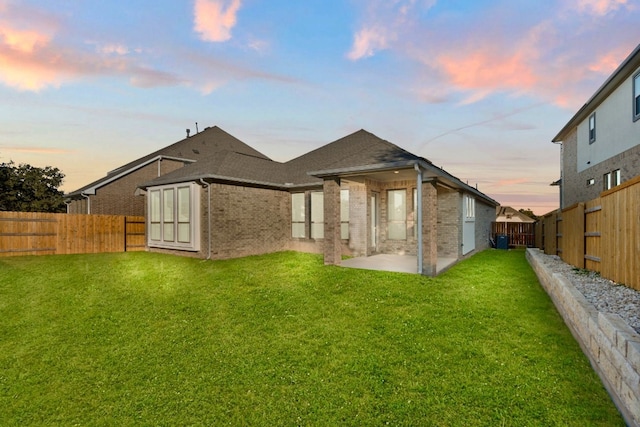 back house at dusk featuring a lawn and a patio