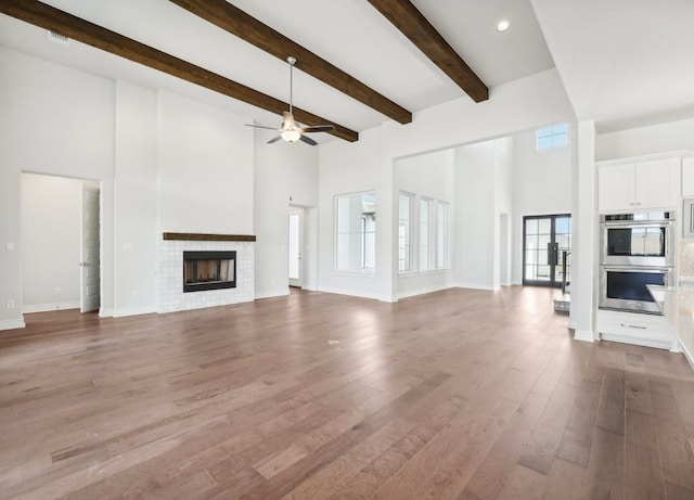 unfurnished living room featuring a fireplace, a towering ceiling, light hardwood / wood-style floors, and ceiling fan