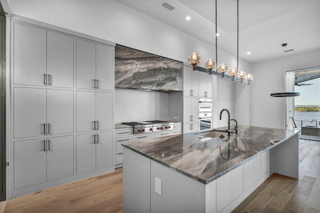 kitchen with dark stone counters, backsplash, hanging light fixtures, light hardwood / wood-style floors, and stainless steel gas stovetop