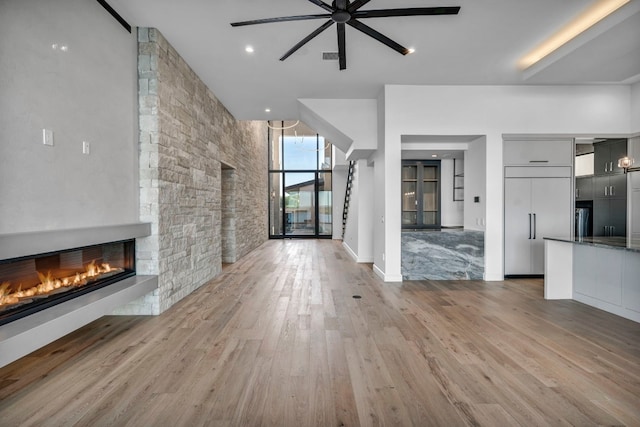 unfurnished living room with ceiling fan, light hardwood / wood-style floors, and a stone fireplace